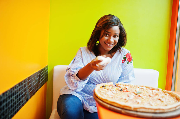 African woman pours salt to pizza while sitting at bright colore - Zdjęcie, obraz