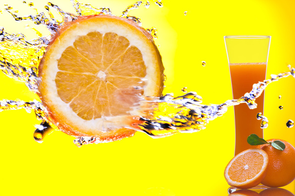 Вид на кусок апельсина, брызгающийся и стакан сока на спине
 - Фото, изображение