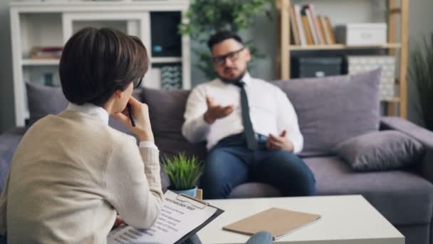 Female psychologist talking to male patient businessman during session in office - Felvétel, videó