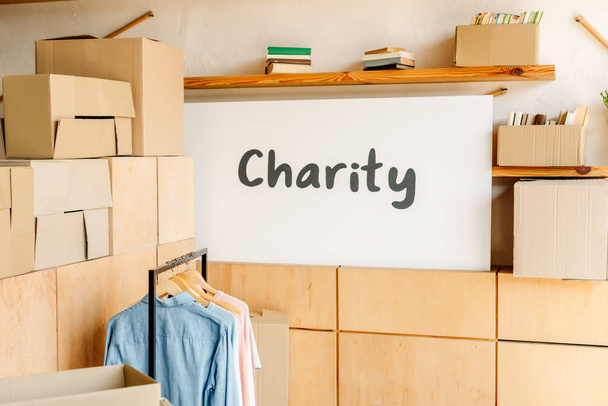 armários de madeira, caixas de papelão, rack com camisas e cartaz com inscrição de caridade
 - Foto, Imagem