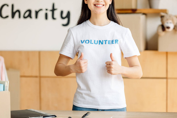 partial view of young woman in white t-shirt with volunteer inscription showing thumbs up  - Photo, Image