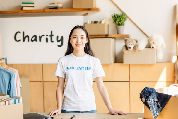 sonriendo chica asiática en camiseta blanca con inscripción voluntaria sonriendo y mirando a la cámara
 - Foto, imagen