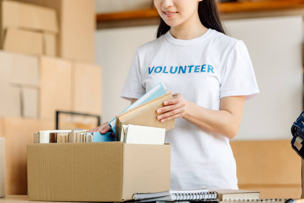 cropped view of young volunteer girl unpacking carton box with books - Foto, Imagem