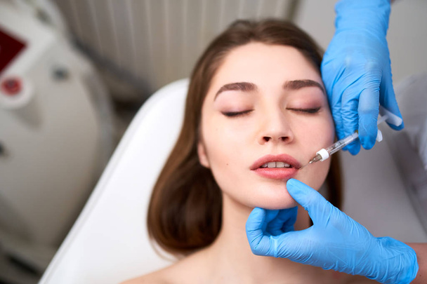 Lip Augmentation. Closeup Of Beautician Doctor Hands Doing Beauty Procedure To Female Lips with Syringe. Young Womans Mouth Receiving Hyaluronic Acid Injection. Cosmetology Treatment. Filler Therapy. - Foto, Imagem