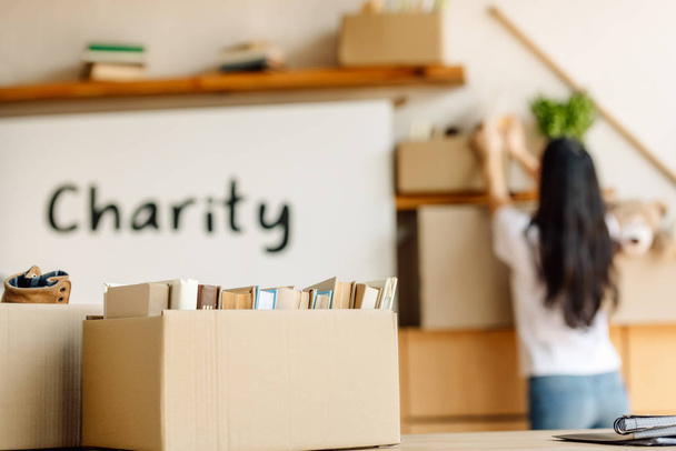 selective focus of cardboard box with books and volunteer working in charity center - 写真・画像