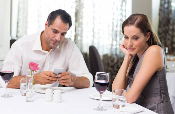 Portrait of a young couple with wine glass and cellphone dining in the restaurant - Photo, image