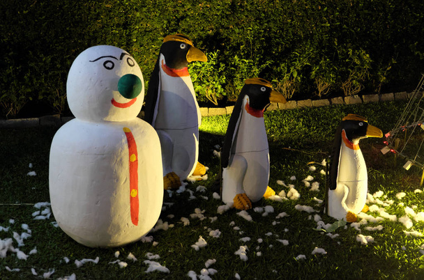 Un bonhomme de neige et trois pingouins maléfiques sont debout sur une pelouse verte. Bonhomme de neige au nez vert. Célébration de Noël dans les pays aux climats chauds
. - Photo, image