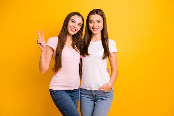 Close up photo two cheerful people beautiful she her ladies models hand arm fingers show v-sign say hi relatives friends hug cuddle embrace wear white pink casual t-shirts isolated yellow background - Foto, Imagen