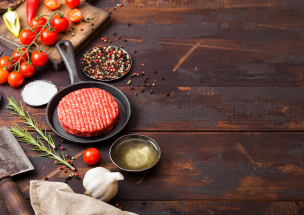 Fresh raw minced homemade farmers grill beef burger in frying pan with spices and herbs and meat hatchet on wooden board. Oil, garlic and tomatoes. - Фото, зображення