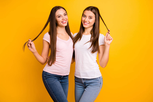Close up photo two people beautiful she her ladies models long straight hairdo playing curls romantic mood toothy smile hugging stand close wear white pink casual t-shirts isolated yellow background - Foto, Imagem