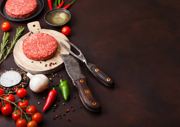 Fresh raw minced homemade farmers grill beef burger on round chopping board with spices and herbs and fork and knife on brown board. Oil, pepper and garlic. - Foto, Imagem