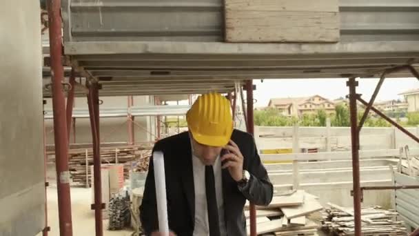Architect talking on cell phone and walking in construction site under building scaffolding. - Felvétel, videó