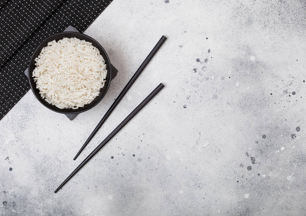 Black bowl with boiled organic basmati jasmine rice with black chopsticks on bamboo placemat on light kitchen table  background. Space for text - Fotoğraf, Görsel