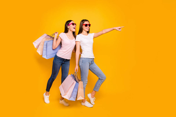 Full length body size view portrait of nice cute charming winsome attractive cheerful straight-haired girls carrying purchase showing far away isolated on bright vivid shine yellow background - Foto, Bild