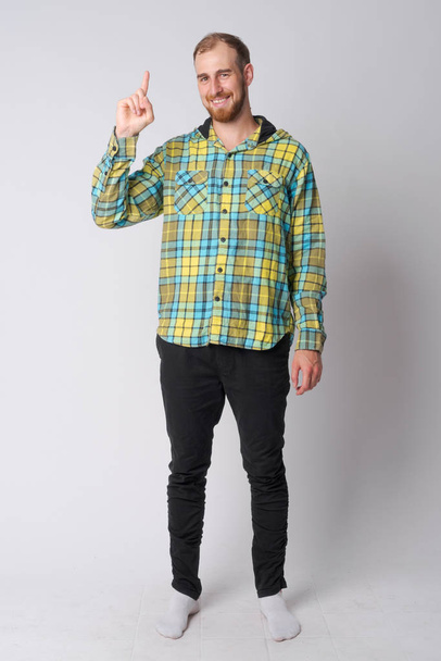 Full body shot of happy young bearded hipster man pointing up - Photo, image
