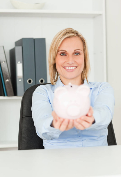 Cute smiling businesswoman holding a piggy bank in her office - Photo, Image
