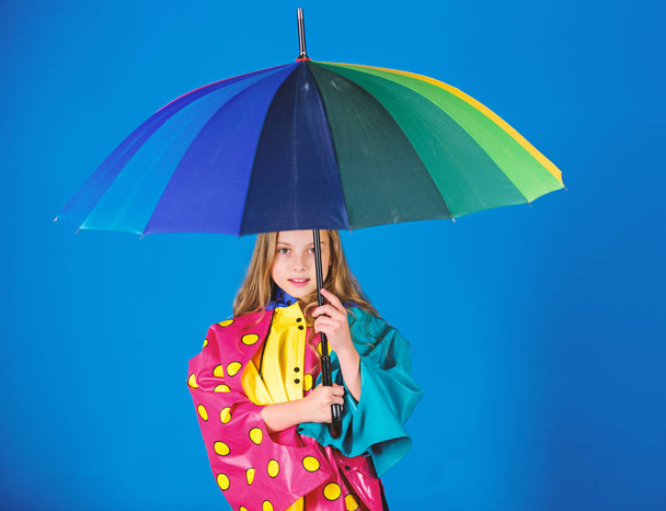 Waterproof accessories manufacture. Enjoy rainy weather with proper garments. Waterproof accessories make rainy day cheerful and pleasant. Kid girl happy hold colorful umbrella wear waterproof cloak - Foto, imagen