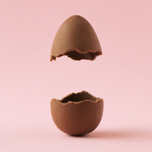 Шоколадне пасхальне яйце розбилося навпіл на пастельно-рожевому тлі. Концепція мінімальних свят Великодня
 - Фото, зображення