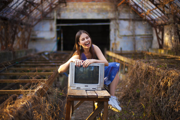 Retrato de arte vintage de una joven sonriente abrazando un televisor analógico retro en una vieja casa abandonada
 - Foto, Imagen
