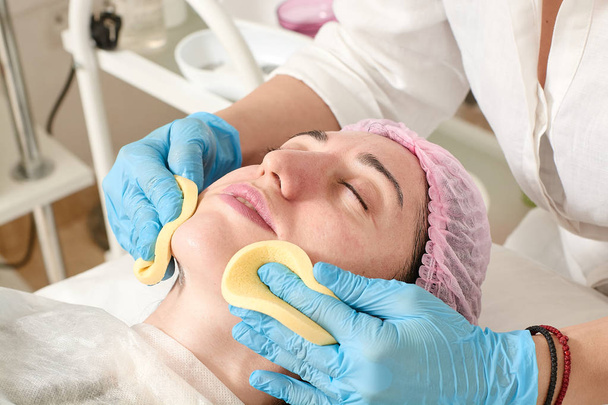 Young woman in beauty salon does skin moisturizing procedure after ultrasound peeling. - Photo, Image