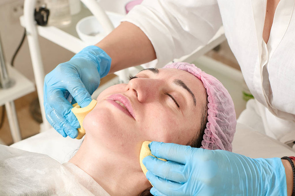 Young woman in beauty salon does skin moisturizing procedure after ultrasound peeling. - Photo, Image