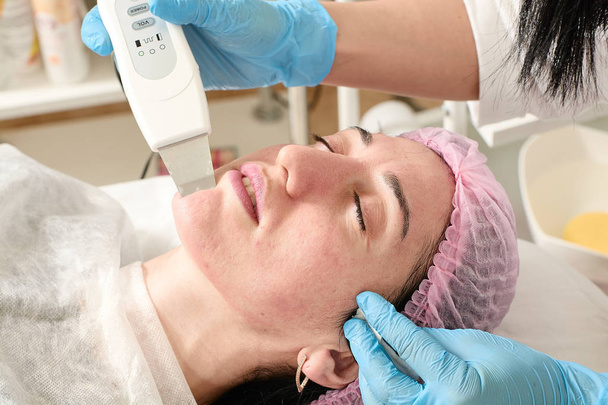 Young woman in beauty salon does ultrasound peeling and facial cleansing procedure. - Photo, Image