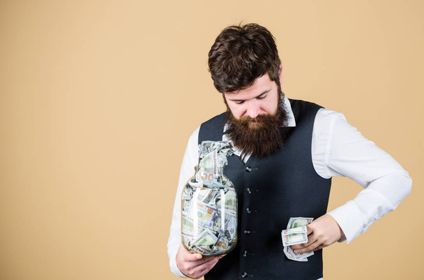 Stuffing some cash into his pockets. Bearded man hiding away cash holdings. Businessman taking cash money out of glass jar. Cash flow budget, copy space - Фото, изображение