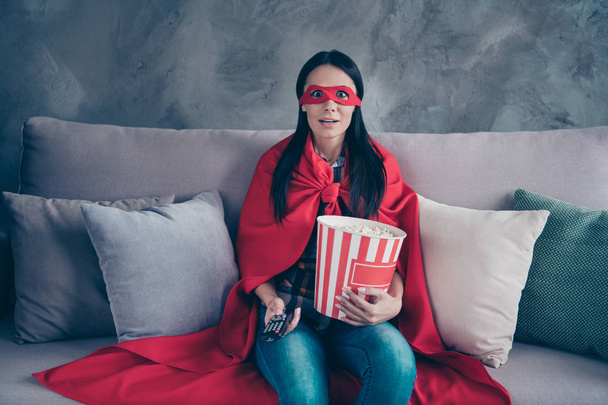 Close up photo beautiful she her superpower lady costume hold popcorn container controller change channels scary movie brave but fear wear red eye mask mantle sit sofa couch divan house indoors - Foto, Imagen