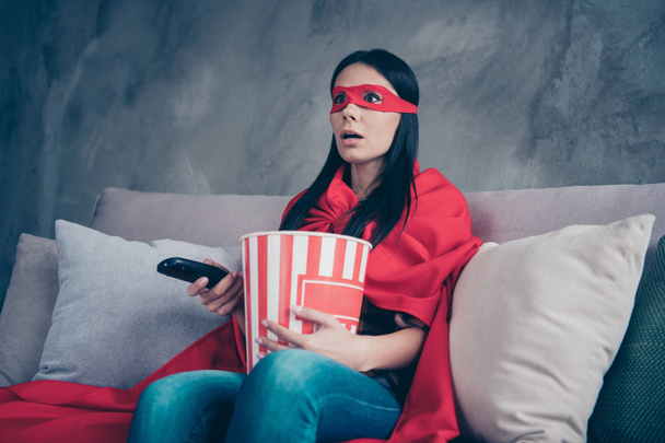 Close up photo beautiful she her superpower lady costume hold popcorn container controller change channels scary movie brave but fear wear red eye mask mantle sit sofa couch divan house indoors - Photo, image