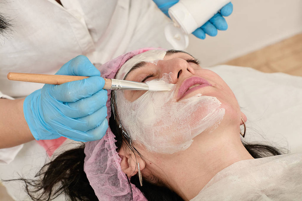 Young woman in beauty salon does make application of moisturizing, softening, regenerating mask. - Фото, зображення