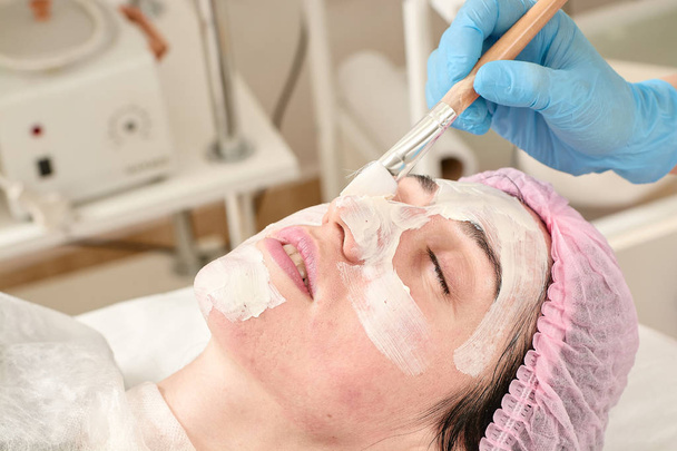 Young woman in beauty salon does make application of moisturizing, softening, regenerating mask. - Photo, Image