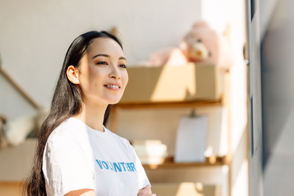 красивая азиатская доброволец улыбается, стоя на солнце и глядя в сторону
 - Фото, изображение