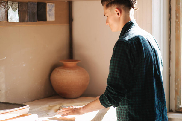 Male potter works with ceramic at his workshop. Handsome young man work inside - 写真・画像