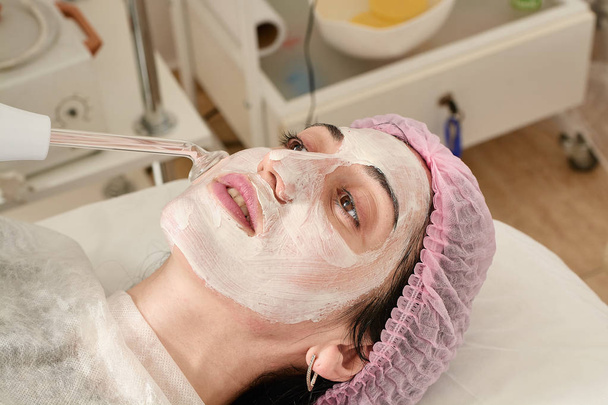 Jonge vrouw in schoonheidssalon doet verjongende, toning procedure darsonval op het gezicht. - Foto, afbeelding