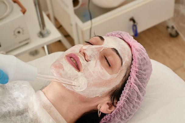 Mujer joven en el salón de belleza hace rejuvenecedor, procedimiento de tonificación darsonval en la cara
. - Foto, imagen