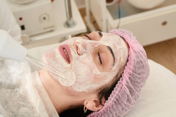 Young woman in beauty salon does rejuvenating, toning procedure darsonval on the face. - Photo, Image