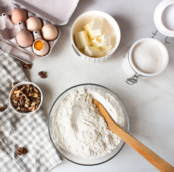 Ingredients for baking cake. Eggs, flour, sugar and whisk, butter nuts.  - Valokuva, kuva