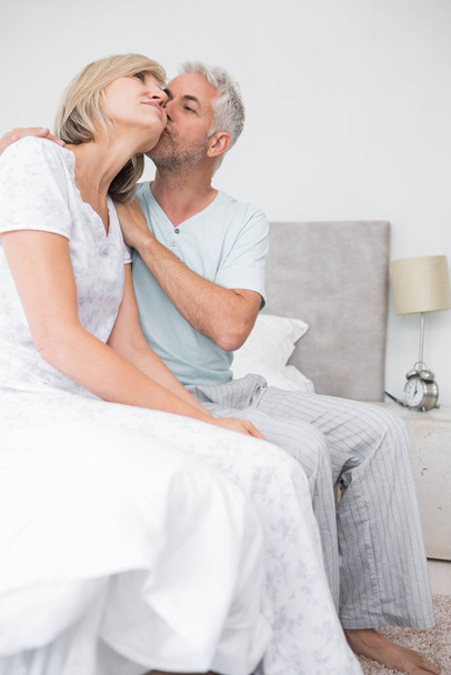 Side view of a mature man kissing womans cheek in bed at the home - Foto, Imagen