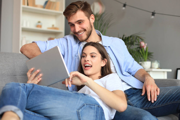 Young couple watching media content online in a tablet sitting on a sofa in the living room. - Fotoğraf, Görsel
