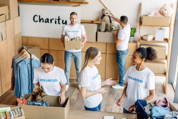 Grupa młodych wolontariuszy wielokulturowych w białych koszulkach z inskrypcjami wolontariuszy pracujących w centrum charytatywnym - Zdjęcie, obraz
