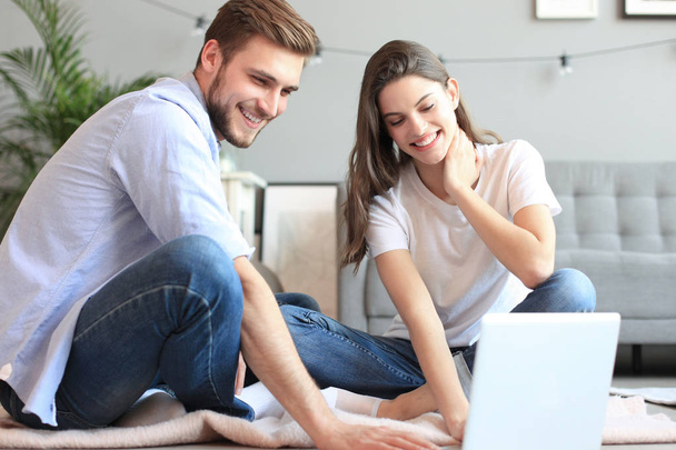 Young couple doing some online shopping at home, using a laptop on floor. - 写真・画像