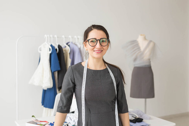 Terzi, moda tasarımcısı ve terzi kavramı - giysi raf elbise arka plan ile genç terzi kadın - Fotoğraf, Görsel