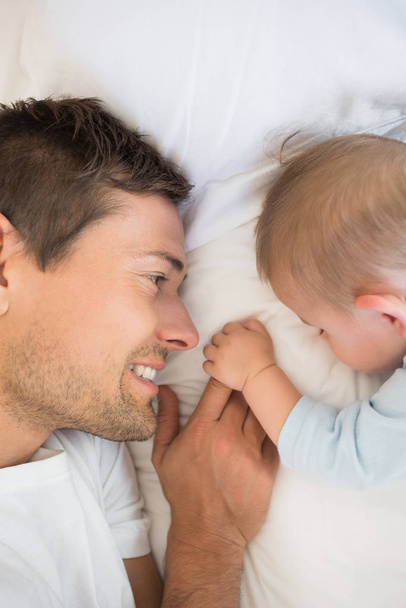 Happy father lying with baby son sleeping at home in bedroom - Fotó, kép