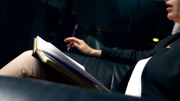 close-up. a woman talks to someone and takes notes in a notebook while sitting in the evening in a black leather chair in the office. The concept of consultation, negotiation. - Foto, Imagen