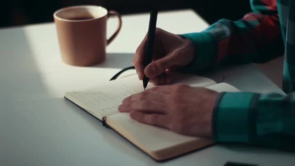 A man writes in a notebook in the early morning at the table with a cup of tea - Záběry, video