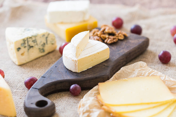 新鮮な食材。チーズ、ブリーチーズ、カマンベール、ブドウ、素朴なテーブル上のナッツ. - 写真・画像