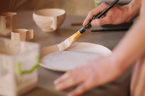Close up of potters hands making ornament on ceramic product. Plate in males hands. Young artist - 写真・画像