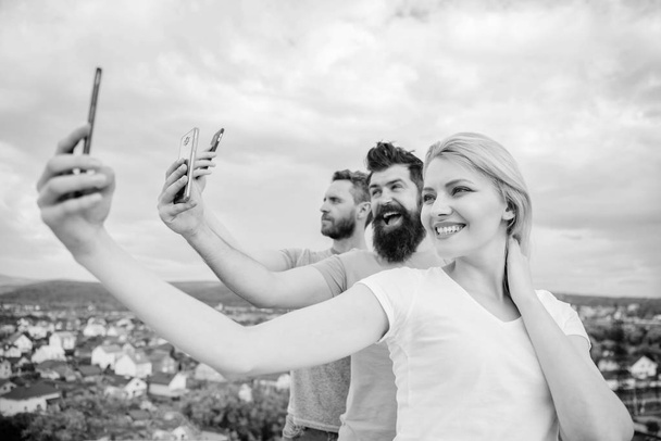 We are all individuals. People enjoy selfie shooting on nature. Best friends taking selfie with camera phone. Sexy girl and men holding smartphones in hands. Sharing selfie on social network - Foto, immagini