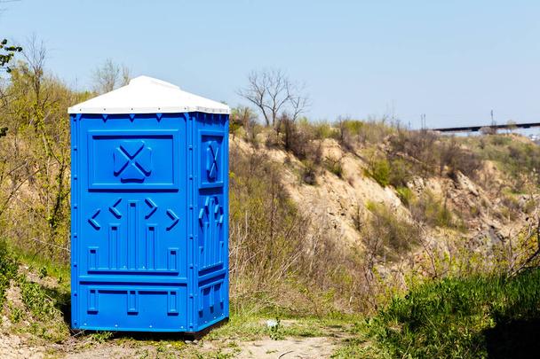 Cabina azul del inodoro Bio en el parque de montaña en el soleado día de verano
. - Foto, imagen