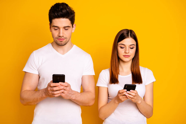 Portrait of his he her she two nice attractive lovely charming stylish trendy focused people using new gadget device isolated over vivid shine bright yellow background - 写真・画像